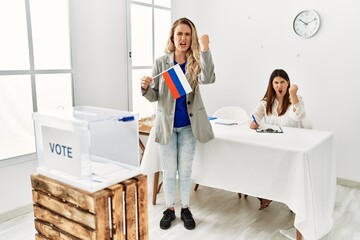 Canvas Print - Young blonde woman at political stand holding russia flag annoyed and frustrated shouting with anger, yelling crazy with anger and hand raised