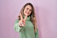 Young Caucasian Woman Standing Over Pink Background Smiling Looking To The Camera Showing Fingers Doing Victory Sign. Number Two.