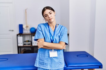 Canvas Print - Young hispanic woman wearing physiotherapist uniform standing at clinic looking sleepy and tired, exhausted for fatigue and hangover, lazy eyes in the morning.