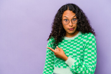 Wall Mural - Young hispanic woman isolated on purple background smiling and pointing aside, showing something at blank space.