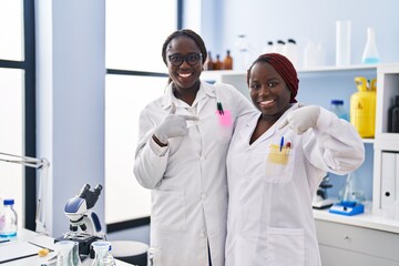 Sticker - Two african women working at scientist laboratory pointing finger to one self smiling happy and proud