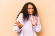 Young hispanic woman isolated on beige background rejecting someone showing a gesture of disgust.