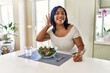 © Krakenimages.com - Young hispanic woman eating healthy salad at home smiling with hand over ear listening an hearing to rumor or gossip. deafness concept.