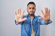 Young hispanic man standing over isolated background doing stop gesture with hands palms, angry and frustration expression