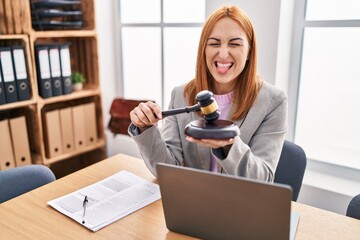 Sticker - Young business woman using gavel sticking tongue out happy with funny expression.