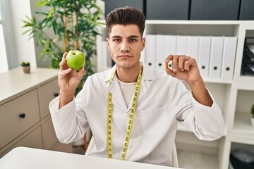 Wall Mural - Young hispanic doctor man holding pills for fat loss relaxed with serious expression on face. simple and natural looking at the camera.