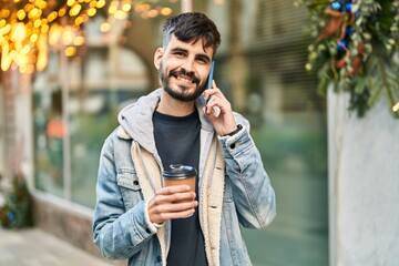 Young hispanic man talking on the smartphone drinking coffee at street