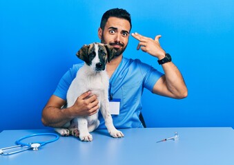 Sticker - Handsome hispanic veterinary man with beard checking dog health shooting and killing oneself pointing hand and fingers to head like gun, suicide gesture.