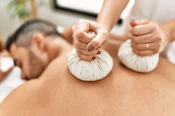 Canvas Print - Young hispanic man having back massage using thai bags at beauty center