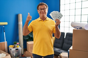 Sticker - Senior man moving to a new home holding money smiling happy and positive, thumb up doing excellent and approval sign