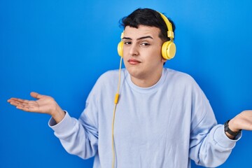 Canvas Print - Non binary person listening to music using headphones clueless and confused expression with arms and hands raised. doubt concept.