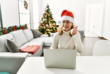 Middle Age Woman Wearing Santa Claus Hat Using Laptop Smiling Happy And Positive, Thumb Up Doing Excellent And Approval Sign