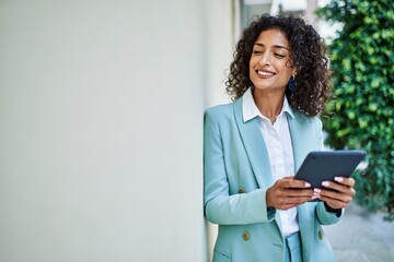 Wall Mural - Young hispanic business woman wearing professional look smiling confident at the city using touchpad device