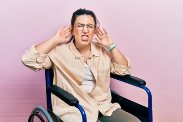 Sticker - Young hispanic woman sitting on wheelchair trying to hear both hands on ear gesture, curious for gossip. hearing problem, deaf