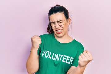 Wall Mural - Young hispanic woman wearing volunteer t shirt very happy and excited doing winner gesture with arms raised, smiling and screaming for success. celebration concept.