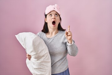 Canvas Print - Woman with down syndrome wearing sleeping mask hugging pillow amazed and surprised looking up and pointing with fingers and raised arms.