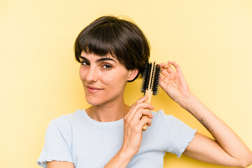 Wall Mural - Young caucasian woman holding a brush hair isolated on yellow background