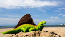Green Colored Plastic Dinosaur On Beach With Blue Sky