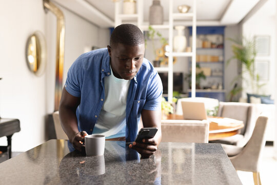 Vertical image of african american man drinking coffee and using smartphone