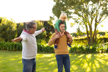 Wall Mural - Image of happy three generation caucasian men walking in garden