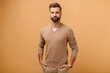 © Vadim Pastuh - Handsome calm brunette man wearing casual clothes looking at camera keeping hands in pockets isolated over beige background