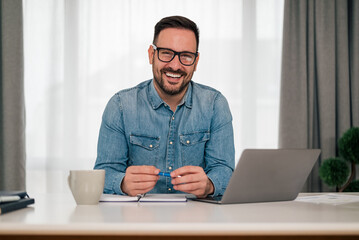 Head shot portrait of smiling successful businessman sitting at workplace desk with laptop