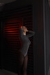 © NASTYA PALEHINA - teen fashion. young brunette girl in a shiny silver bodysuit is standing fashion in profile with hands near head on the black iron wall background with red light. fashion concept, free space