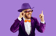 Overjoyed man entertainer in suit and hat isolated on purple studio background point up at sale deal or offer. Smiling funny male performer or partyman recommend entertainment. Party and fun.