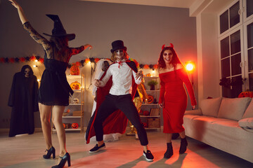 Wall Mural - Happy adult people dancing and enjoying loud music all together at friendly gathering on Halloween. Funny young man dressed up in vampire cloak having fun at festive party with friends late at night