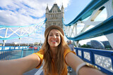 Fototapeta Londyn - Smiling girl takes selfie photo on Tower Bridge in London, United Kingdom