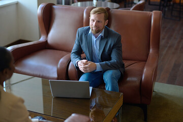 Aufkleber - Young confident businessman in formalwear communicating with African American female colleague while sitting in leather armchair