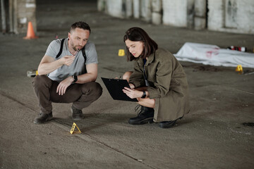 Wall Mural - Policeman showing evidence in metal pincers to his female colleague making notes in document during crime scene investigation