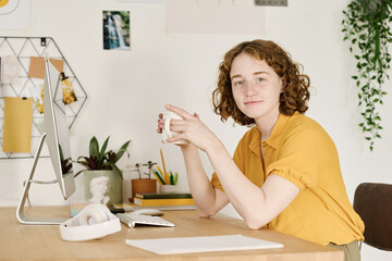 Aufkleber - Happy young female freelancer or home office worker having tea or coffee while sitting by workplace in front of computer monitor