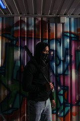 Wall Mural - Side view of african american hooligan in mask and hoodie holding baseball bat near graffiti on wall