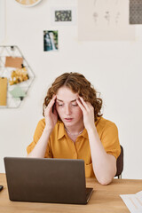 Poster - Young businesswoman expressing misunderstanding or tiredness while sitting by desk in front of laptop and looking through online data