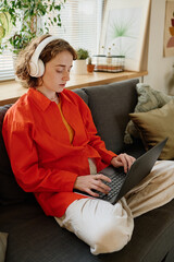 Aufkleber - Young serious businesswoman or student in headphones and casualwear sitting on couch with laptop on her crossed legs and networking