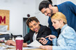 © ADDICTIVE STOCK - Cheerful multiethnic colleagues browsing smartphone during paperwork