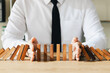 © Thapana_Studio - Risk management, business man hand Stop the continuous falling of wooden dominoes, stop the impact of the business crisis. hedging Solving business problems for success.