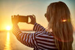 Woman traveler tourist using smartphone, taking photo of sea view at sunset in summer day. Enjoying European, Famous popular touristic place in world.