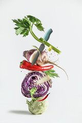 Wall Mural - Various colorful vegetables and knife balancing at white background. Creative food concept with healthy ingredients.