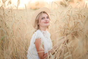 A young girl in a white dress in yellow wheat in the summer at sunset.