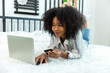 © kanpisut - Young woman consumer holding credit card and laptop buying online at home. Woman shipping online with credit card in hand. Women using laptop technology paying credit card shopping online