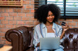 © kanpisut - Young woman consumer holding credit card and laptop buying online at home. Woman shipping online with credit card in hand. Women using laptop technology paying credit card shopping online
