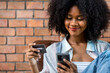 © kanpisut - Young woman consumer holding credit card and smartphone buying online at home. Woman shipping online with credit card in hand. Women using smartphone technology paying credit card shopping online
