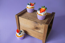 Beautiful Photo Of A Delicious Cupcake, Desert With Strawberry And Blueberries In A Lilac Stand With White Polka Dots, On A Purple Background, On A Wooden Box