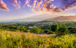 © Yaroslav - view from hill with golden grass and green bushes to a valley town with majectic mountains and scenic cloudy sunset on background