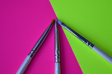 Poster - Professional cosmetic makeup brushes of different sizes on a pink and green background for applying powder, shadows and blush and other cosmetic products