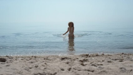 Wall Mural - Happy woman coming out ocean splashing water. Girl running to sand seashore.