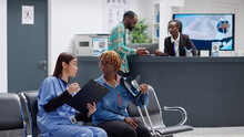 African American Woman With Crutches Suffering From Physical Impairment, Talking To Medical Assistant Abour Disability And Recovery. Diverse People Discussing In Hospital Reception Area.