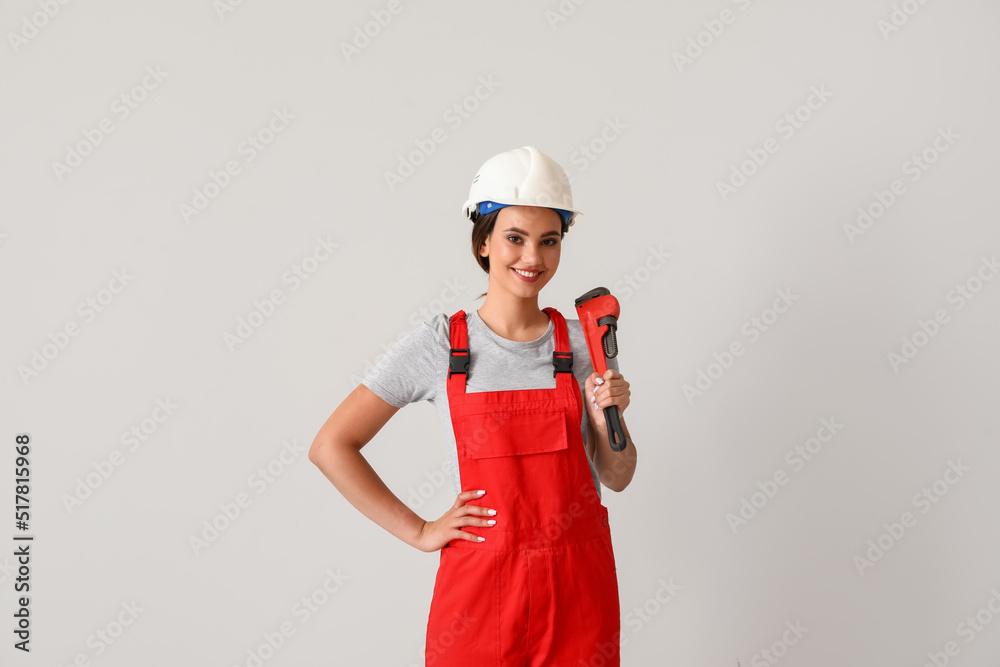Female plumber with pipe wrench on light background